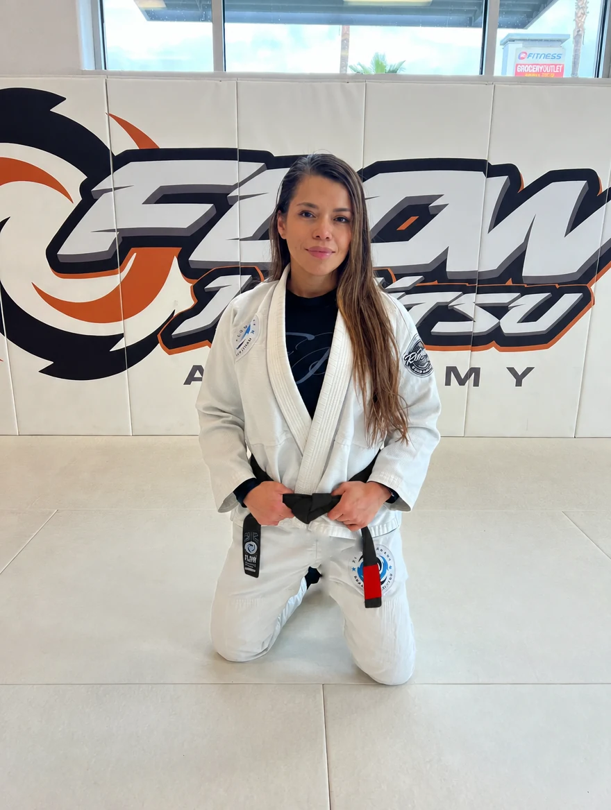 Zaide Oropesa kneeling on the mat in a white gi and black belt in front of the orange Flow wall logo