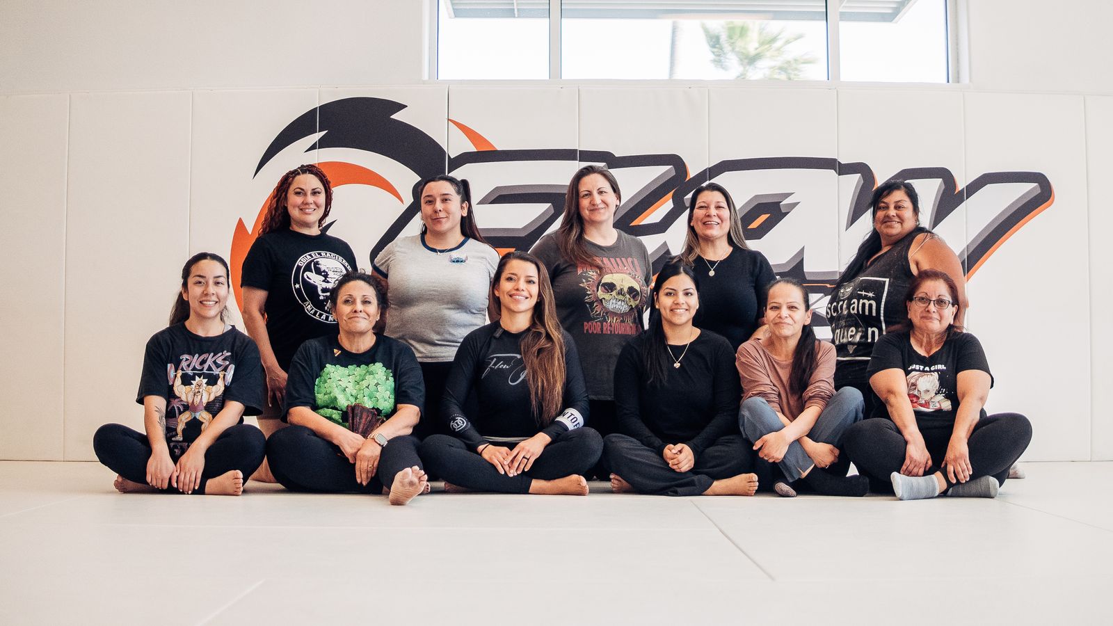 A large group of women sitting and standing together on the mat in front of the orange Flow wall logo