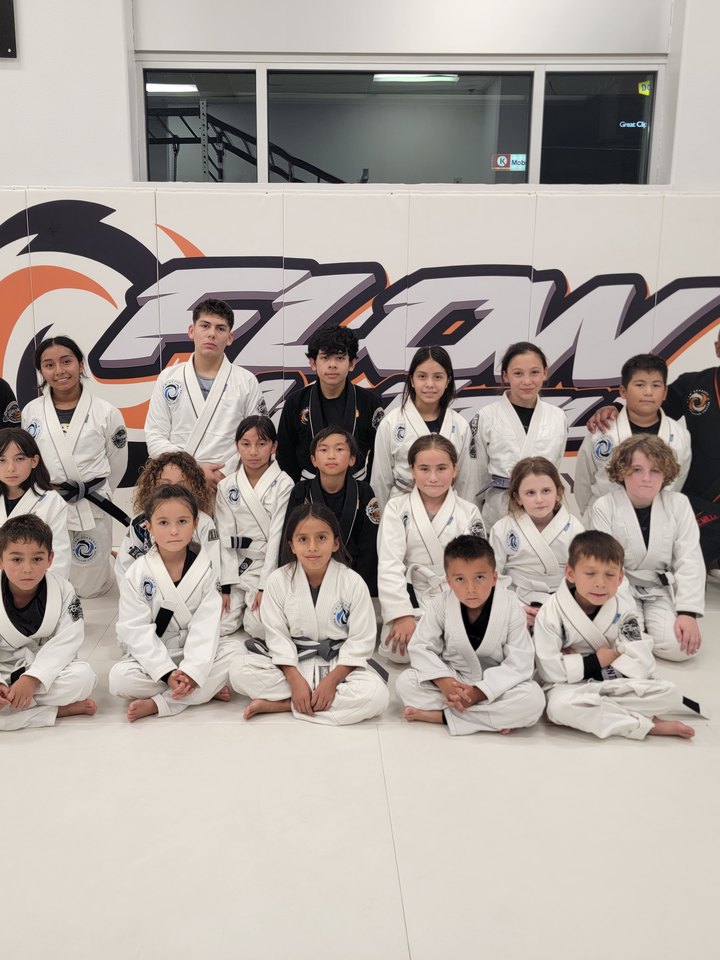 Flow Academy Riverside youth students in gis together in front of the Flow wall logo