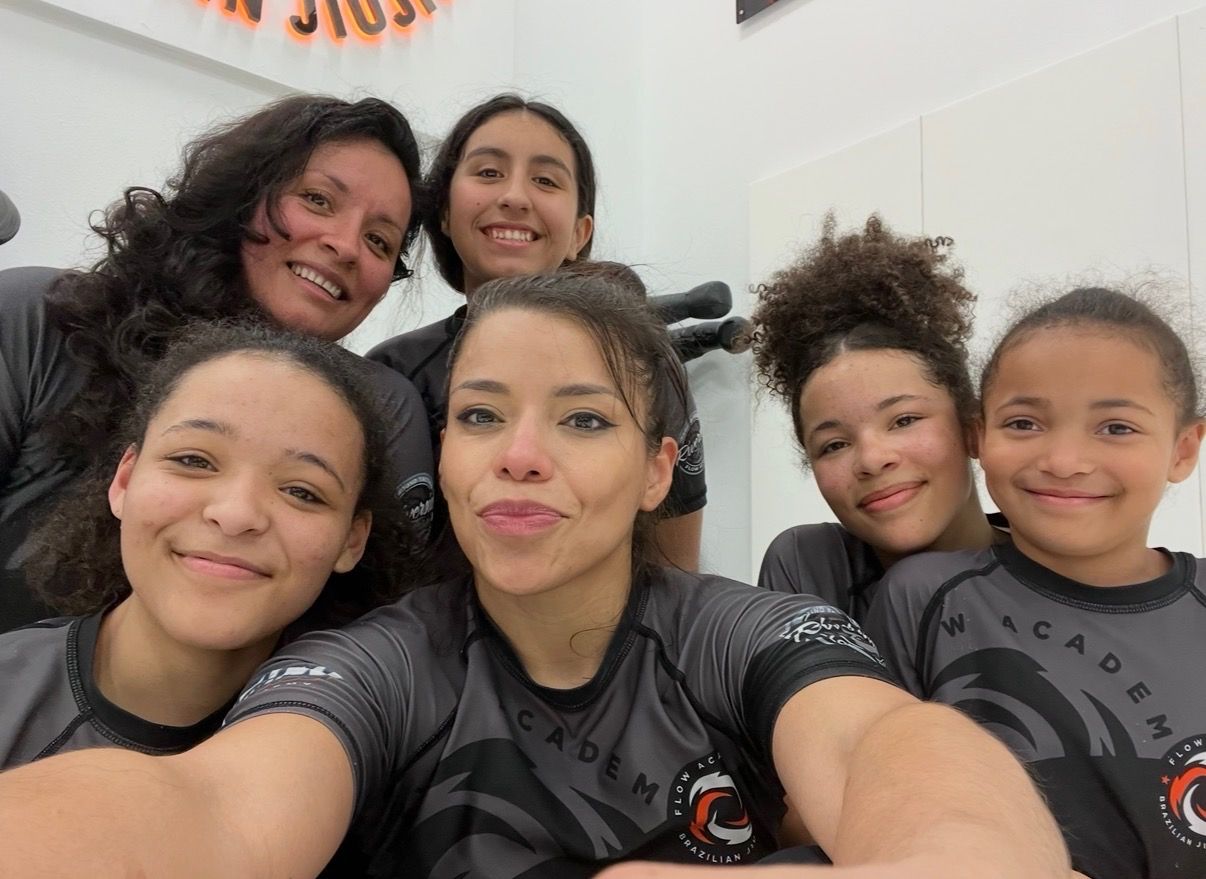 Professor Zaide with students, women and girls of different ages in matching Flow rash guards, smiling together in a selfie
