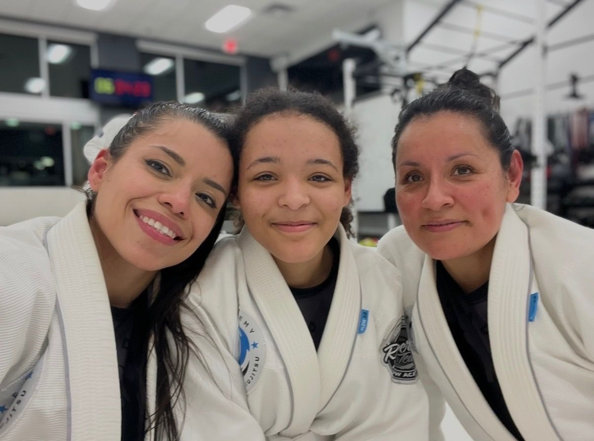 Zaide smiling with a teenage girl and a woman, all three in white gis